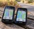 Garmin and iGPSPORT GPS cycling computers displayed side by side on a wooden bench.